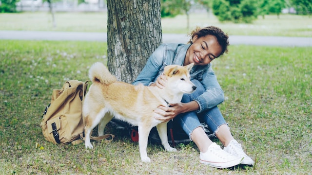 Puppy and owner sitting together under a tree in a grass field
